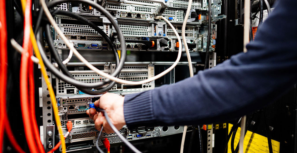 Technicien IT français effectuant la maintenance d'un switch réseau dans une armoire technique avec outils spécialisés